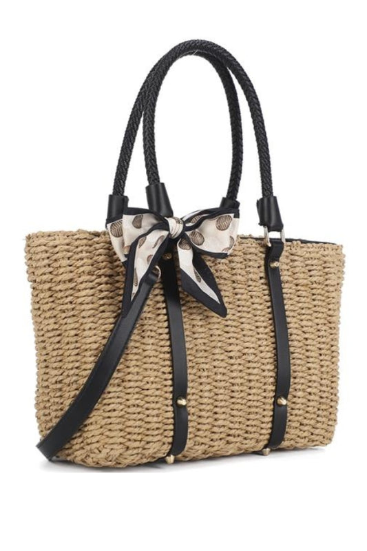 Woven straw handbag with black handles and a decorative bow on a white background