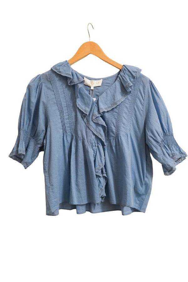 Denim blouse with ruffled details on a wooden hanger against a white background