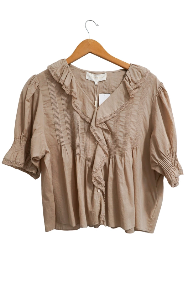 Taupe blouse with ruffled details on a wooden hanger against a white background