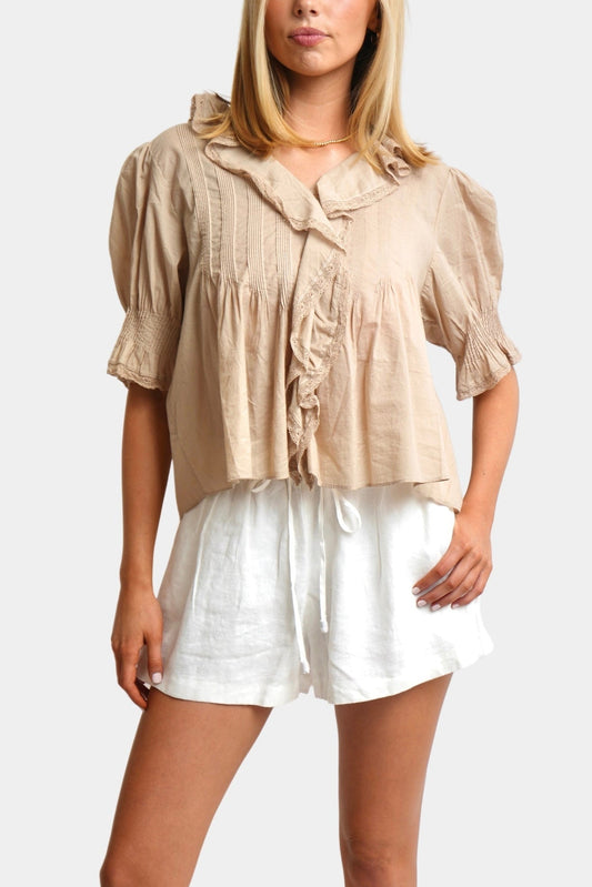 Woman wearing a beige top and white shorts on a plain background