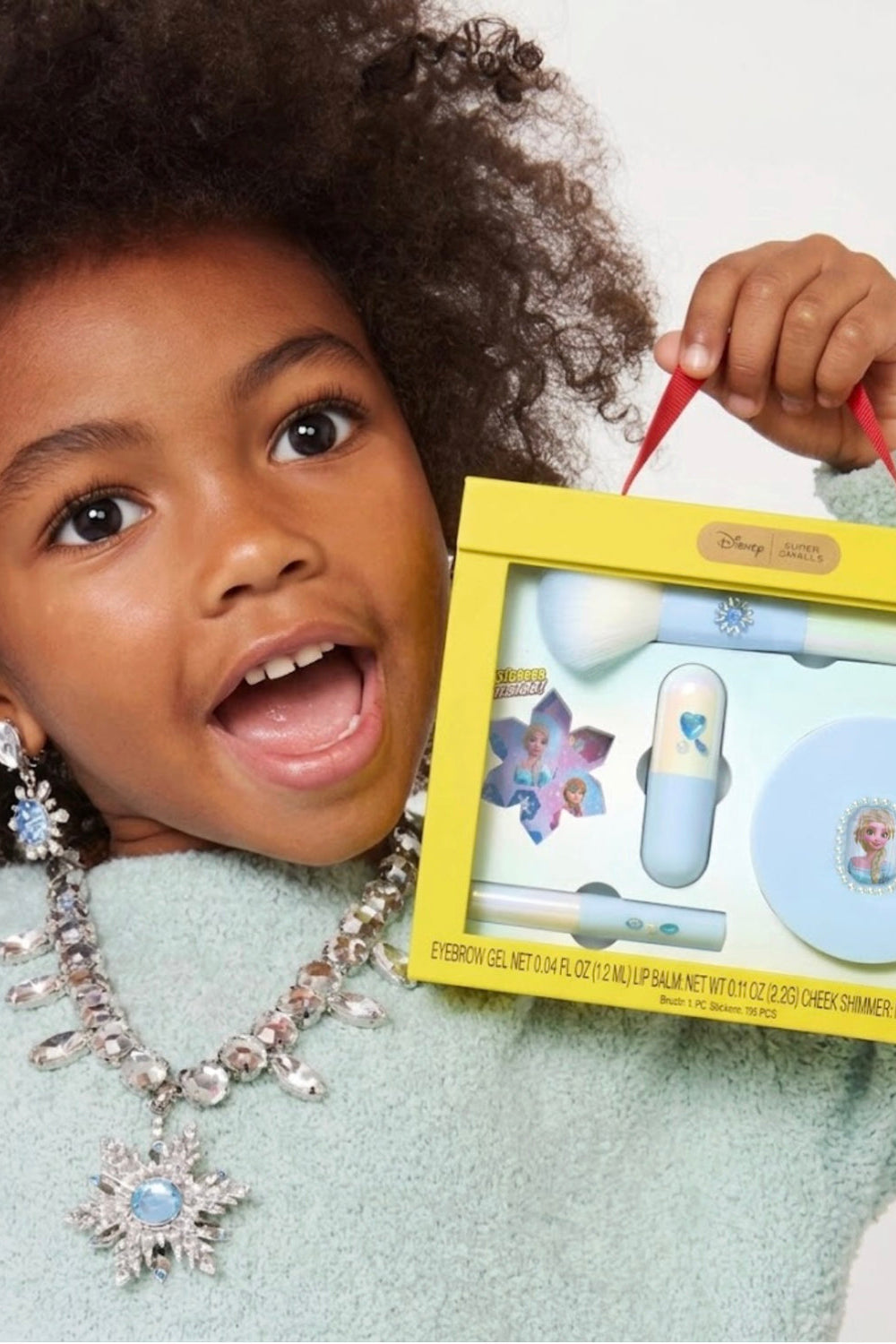 Frozen Elsa makeup kit held near a child’s face, showing brush and compact