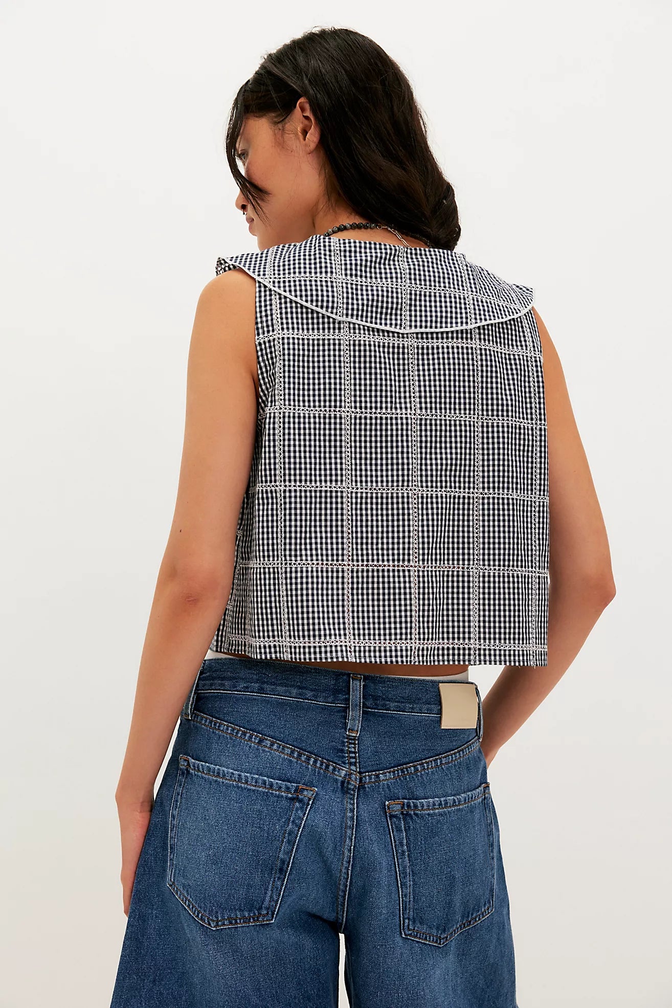 Person wearing a checkered vest and blue jeans on a white background