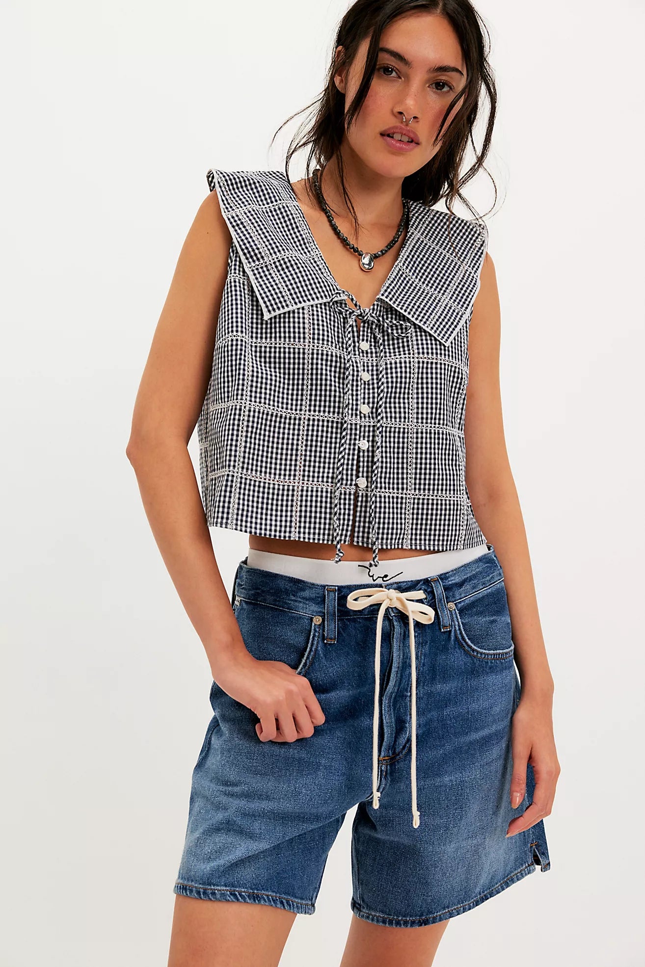 Woman wearing a checkered sleeveless top and denim shorts on a white background