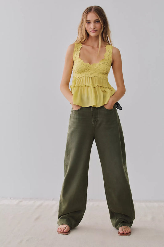 Woman wearing a yellow peplum top and olive green pants against a plain background