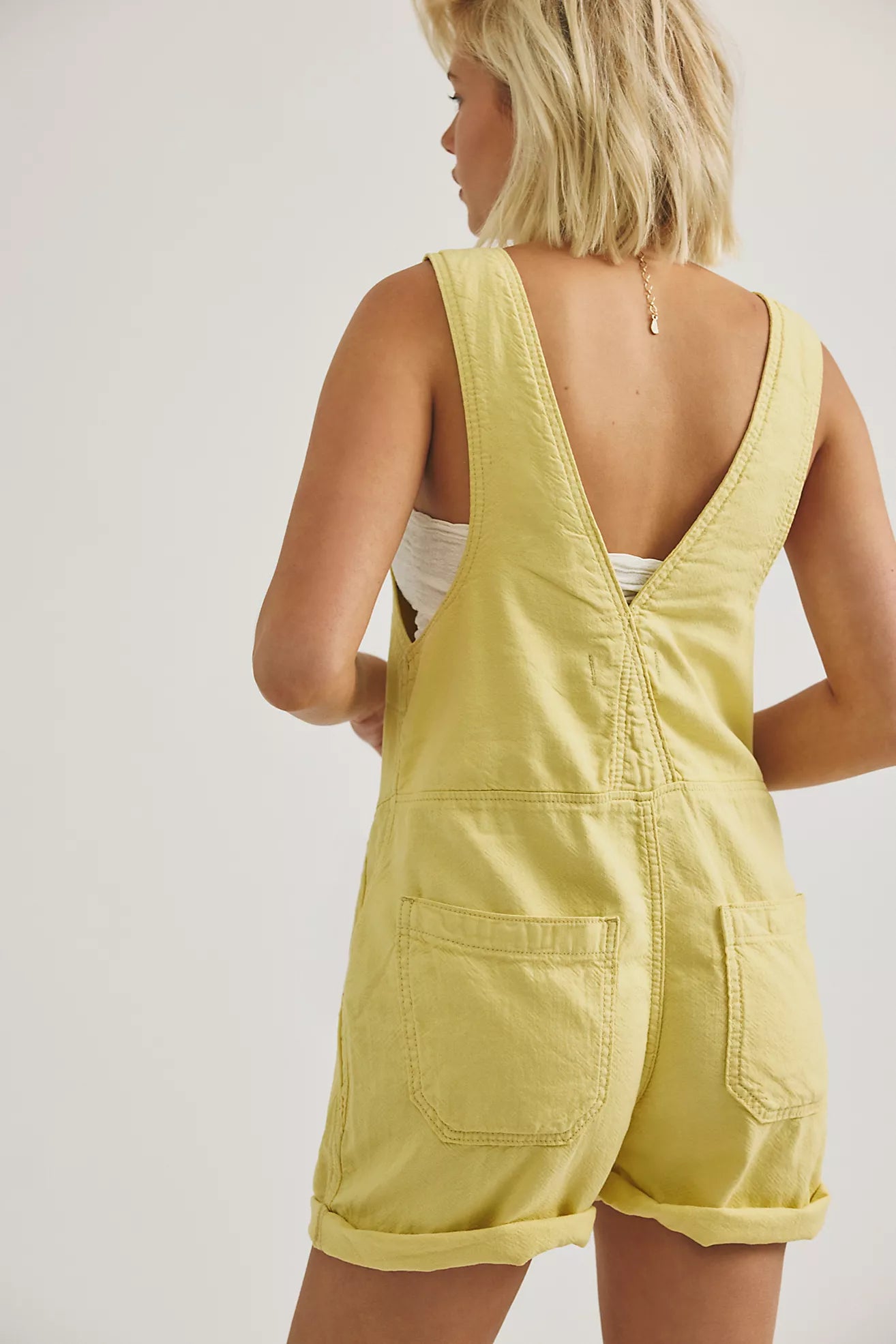 Sleeveless yellow shortall back view with open V yoke and patch pockets