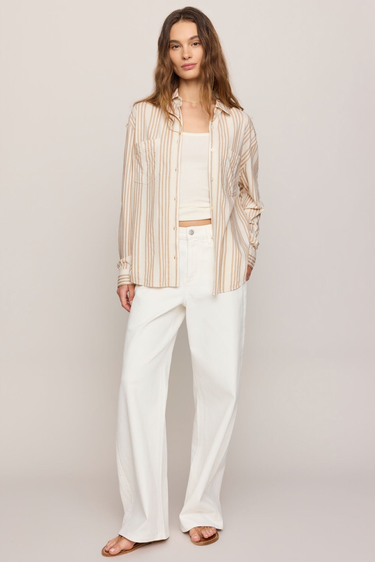 Striped button-up shirt worn over white wide-leg pants, long sleeves