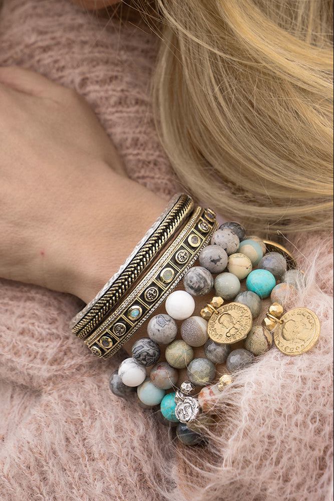 Gold bangle cuff with dark-blue stones and engraved border, worn with beaded layers