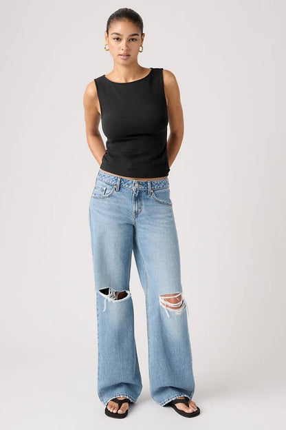 Person wearing a black tank top and shakey ground light blue jeans with a white background