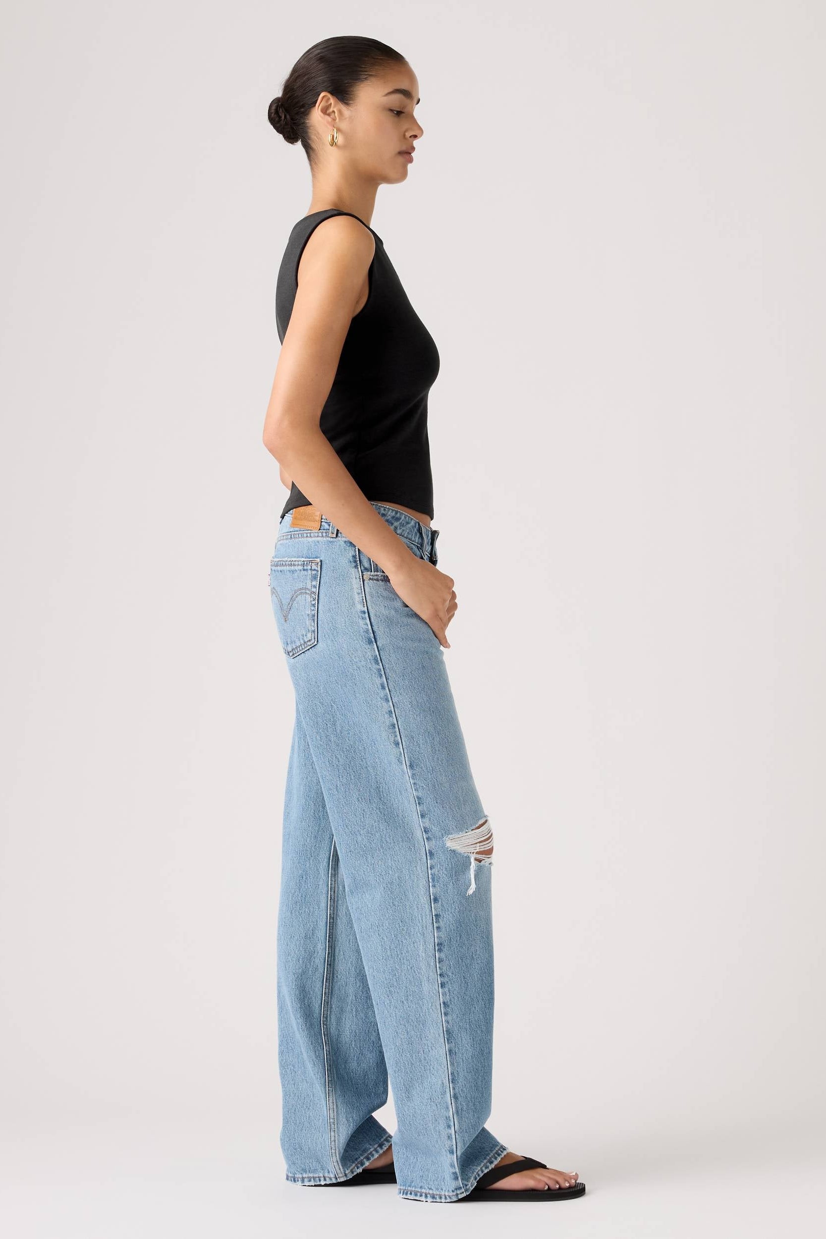 Person wearing light blue jeans and a black top on a white background