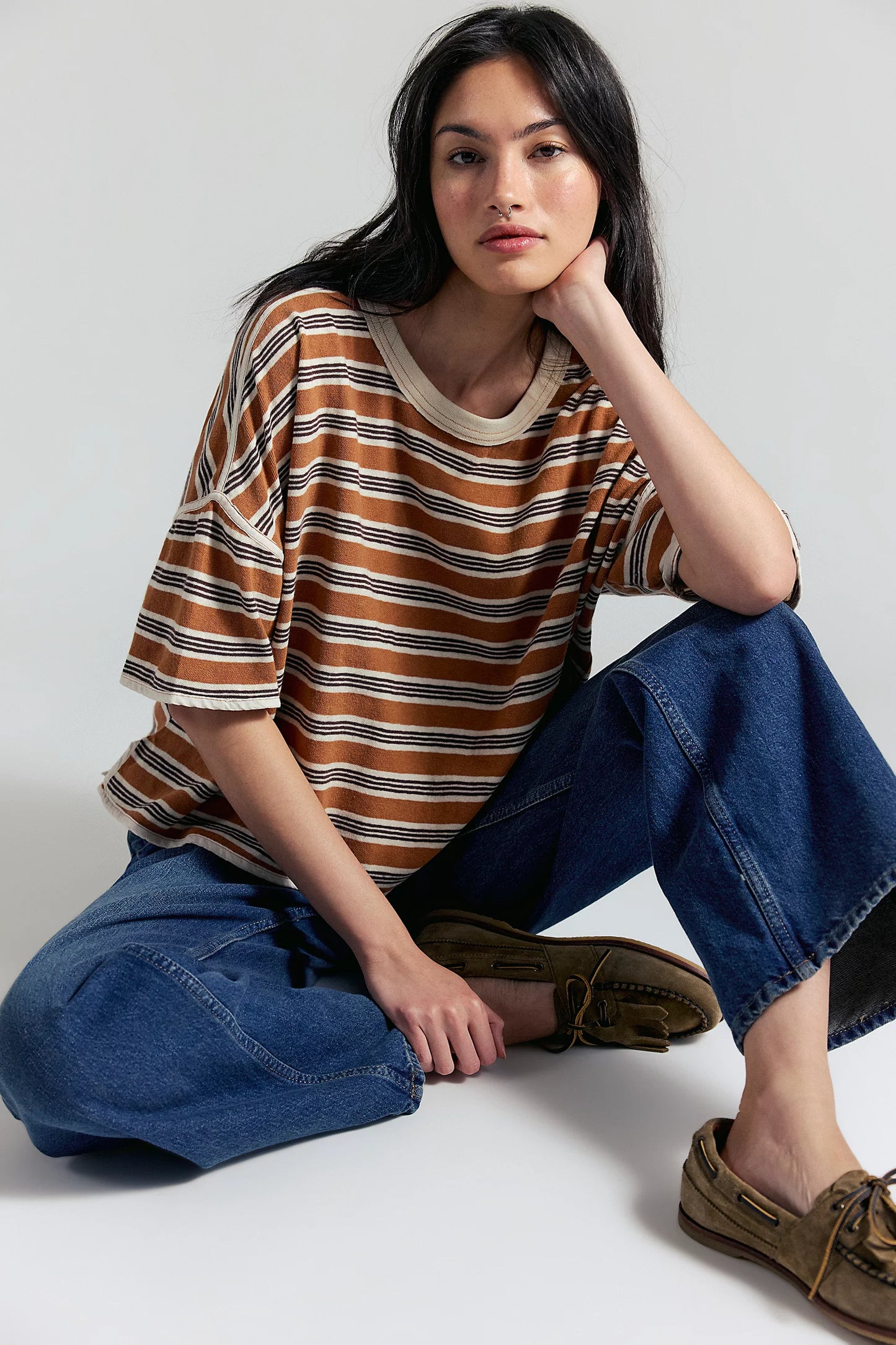 Woman wearing a striped shirt and jeans sitting on a white floor.