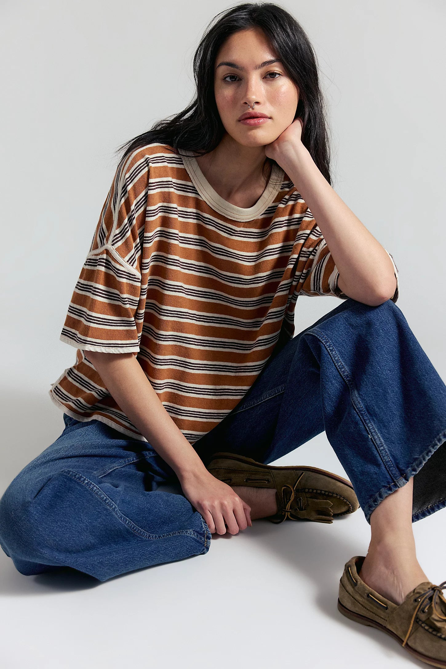 Woman wearing a striped shirt and jeans sitting on a white floor.
