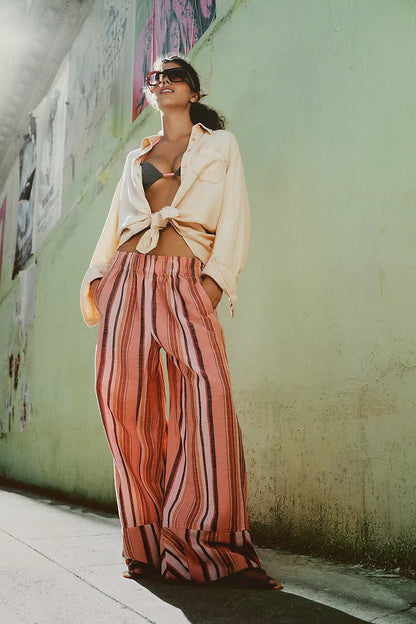Woman in a casual outfit with a beige jacket and striped pants against a graffiti-covered wall.