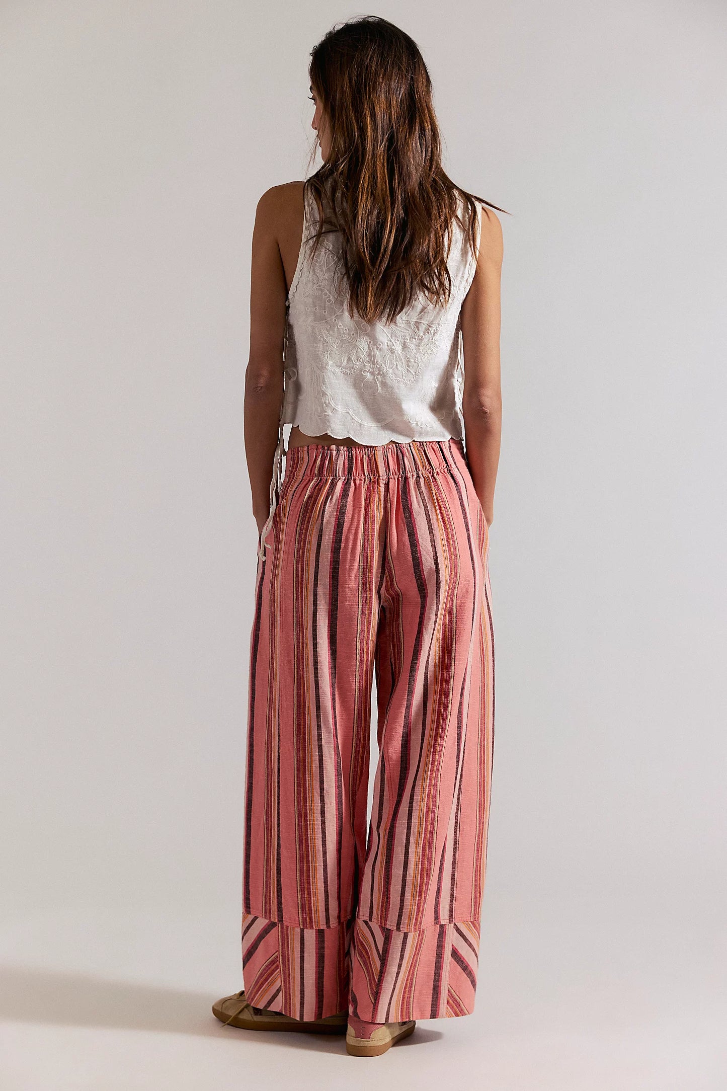 Woman wearing a white sleeveless top and red striped pants on a plain background