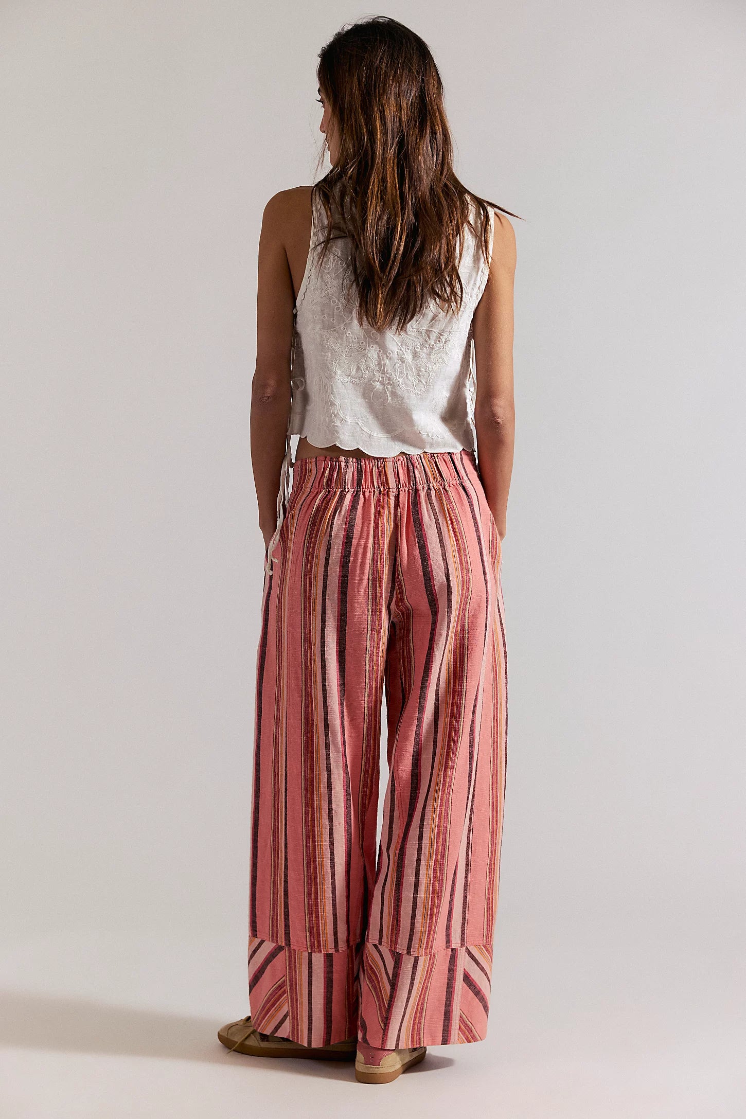 Woman wearing a white sleeveless top and red striped pants on a plain background