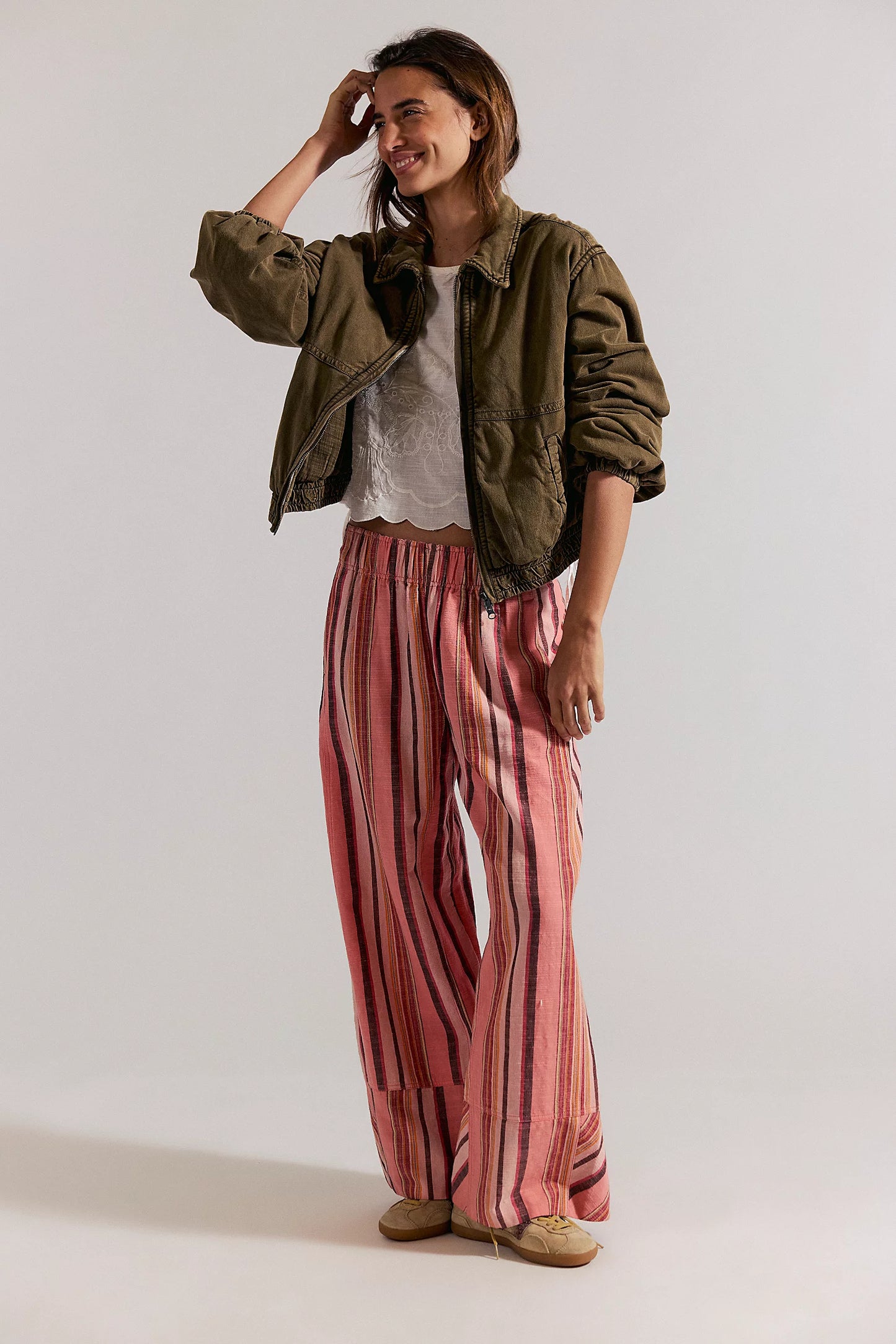 Woman wearing a green jacket, white shirt, and pink striped pants on a white background
