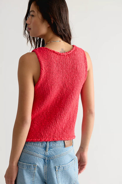 Person wearing a red knitted tank top and blue jeans against a white background