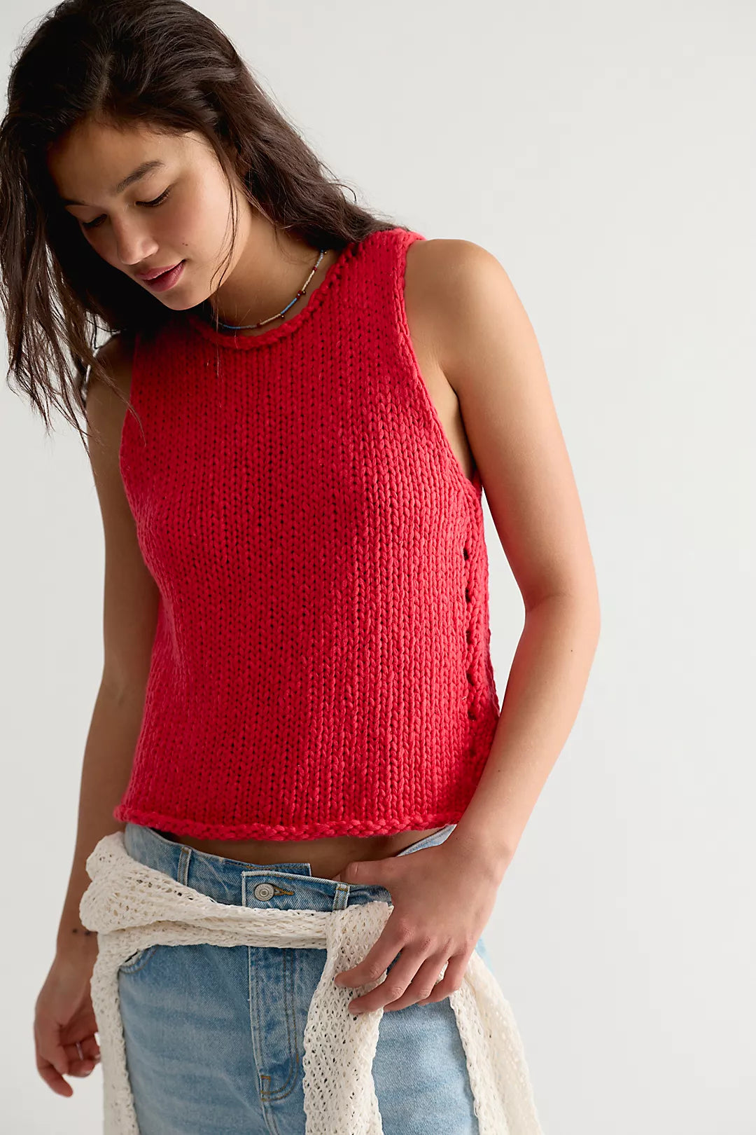 Woman wearing a red sleeveless knitted top against a plain background