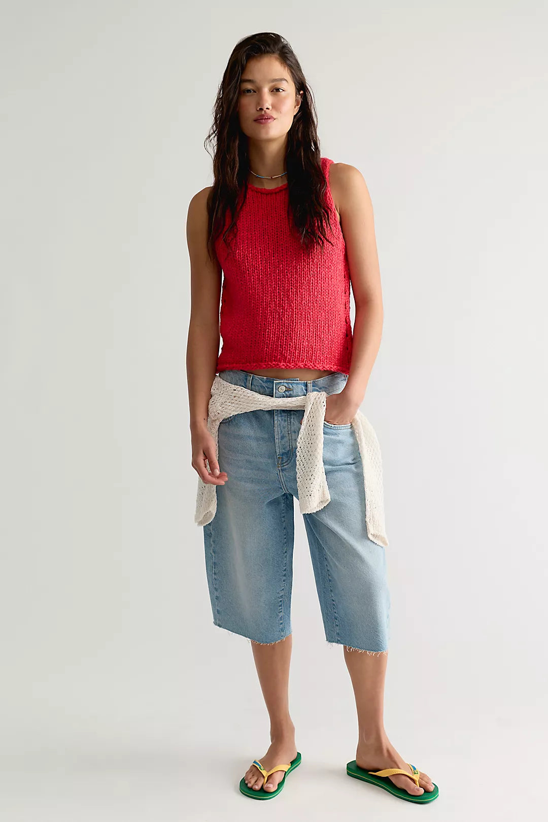 Woman wearing a red sleeveless top and blue denim shorts on a white background