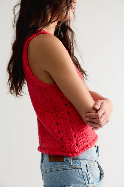 Person wearing a red knitted tank top and blue jeans against a white background