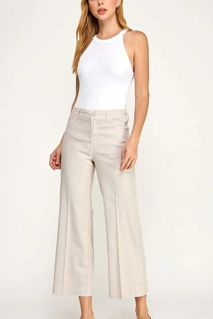 Woman wearing a white sleeveless top and beige wide-leg pants on a white background