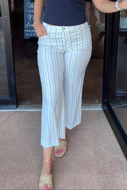 Person wearing white pinstripe pants and a navy top, standing in front of a glass door.
