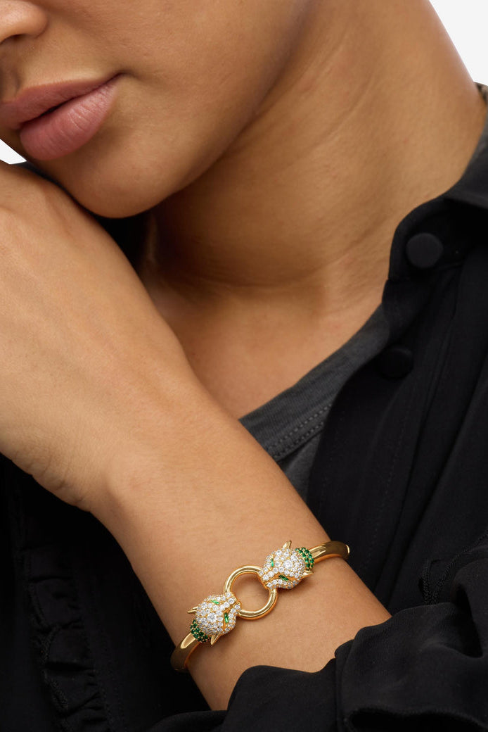 Gold cuff bracelet on wrist with linked loop design, clear crystals and green stones