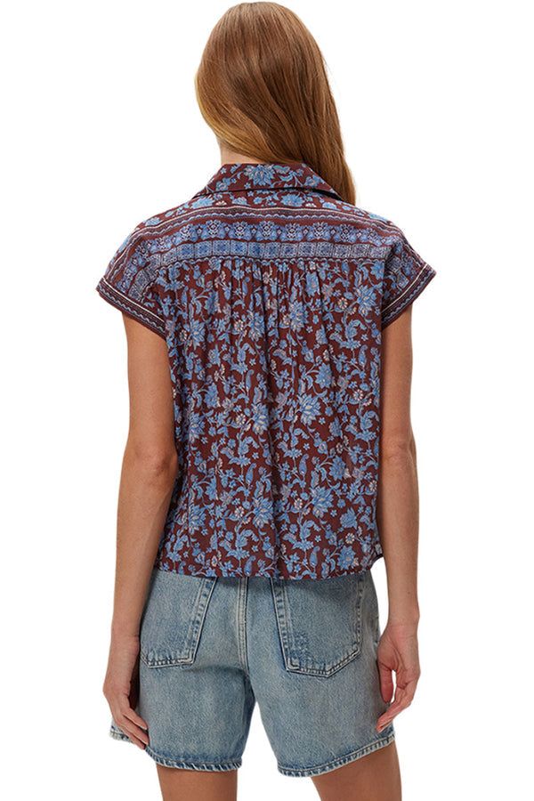 Woman wearing a sleeveless patterned top and denim shorts on a white background