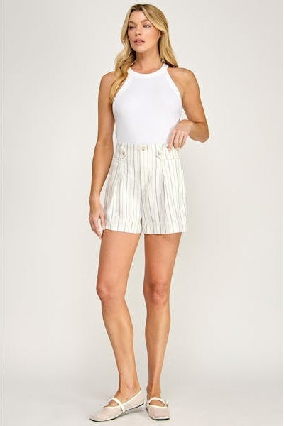 Woman wearing a white sleeveless top and striped shorts on a plain background