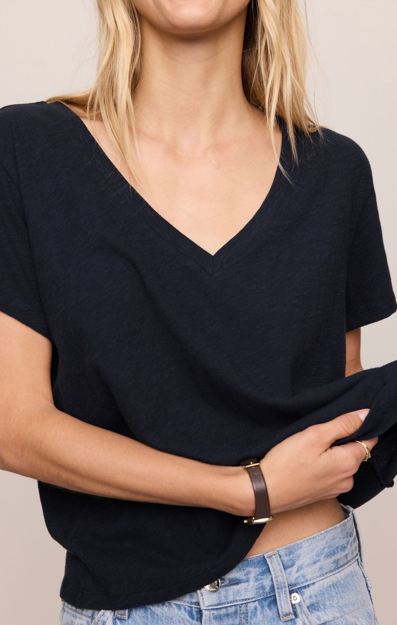 Person wearing a black V-neck top and blue jeans against a neutral background