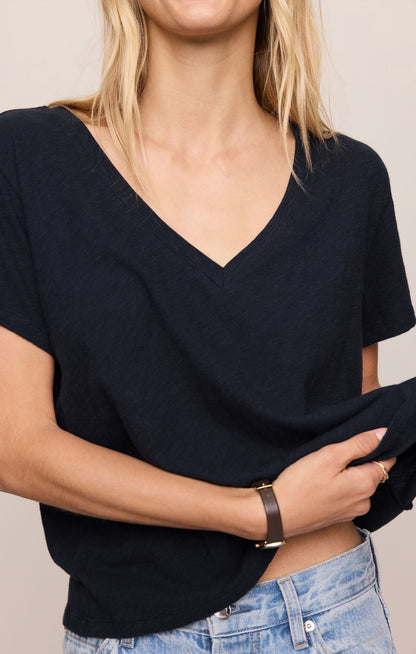 Person wearing a black V-neck top and blue jeans against a neutral background