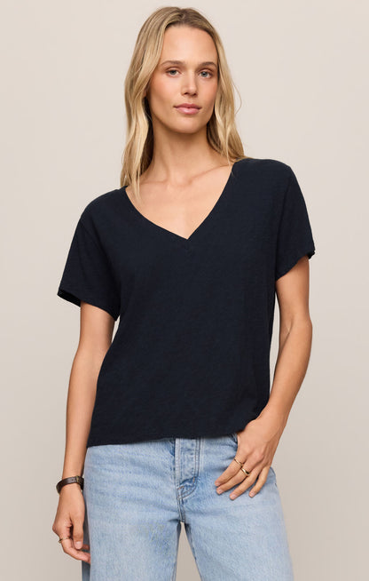 Woman wearing a black V-neck t-shirt and light blue jeans on a beige background
