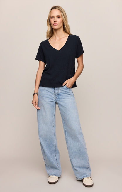 Woman wearing a black V-neck shirt and light blue jeans on a plain background