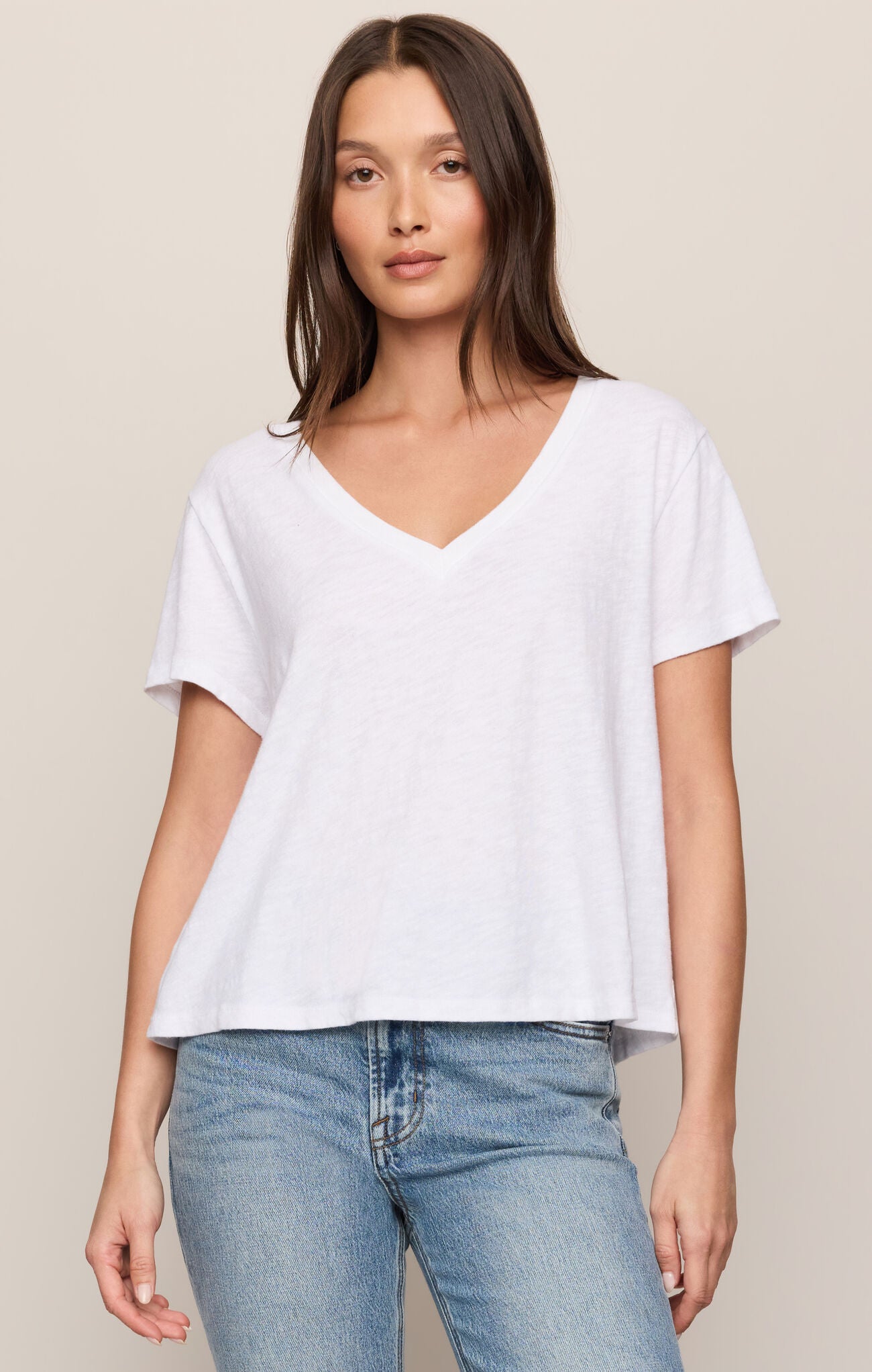 Woman wearing a white t-shirt and blue jeans against a beige background