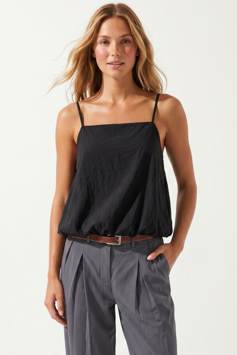 Woman wearing a black billowy bubble hem top and gray pants on a white background
