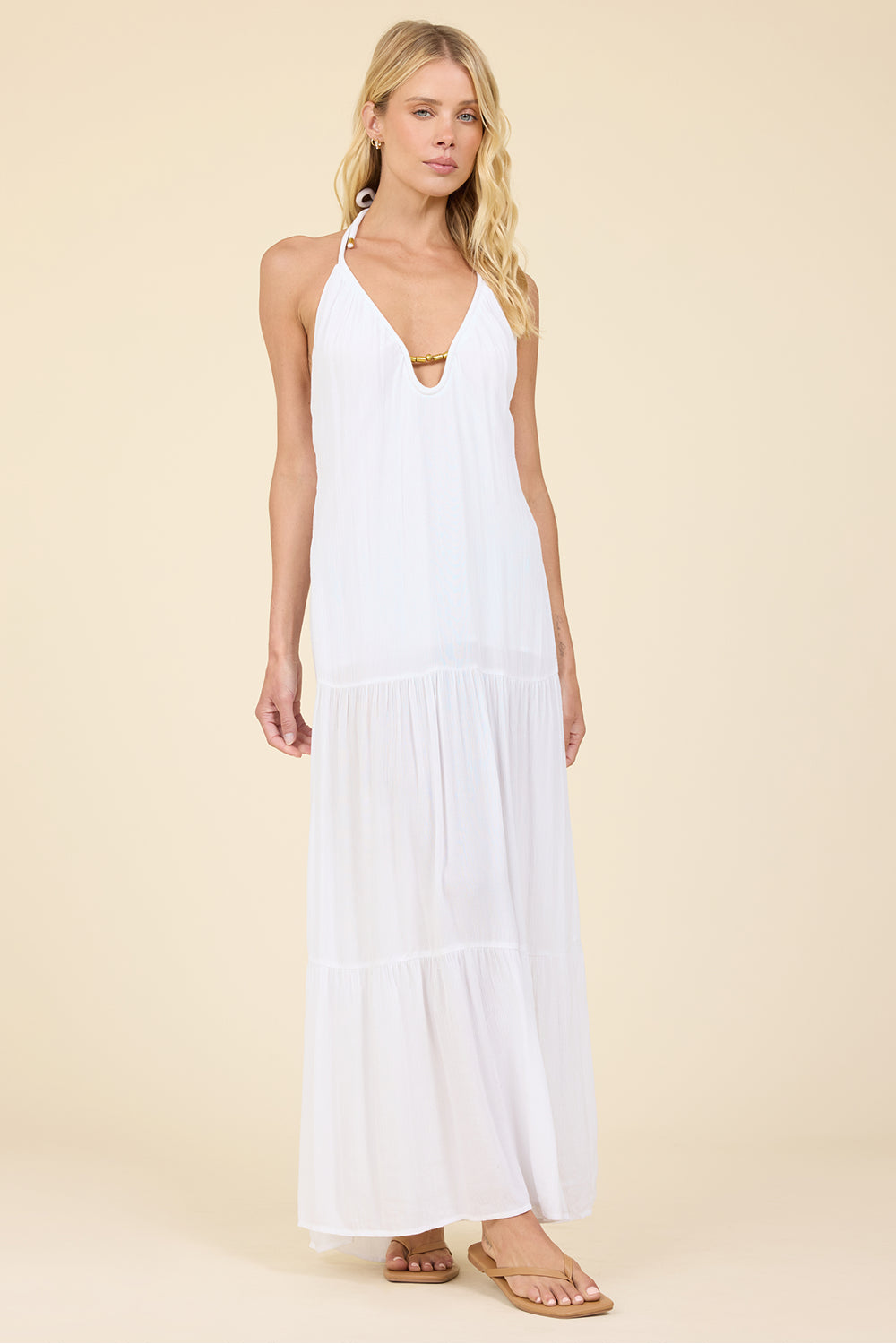 Woman wearing a white halter neck dress  with gold trim detail on a beige background