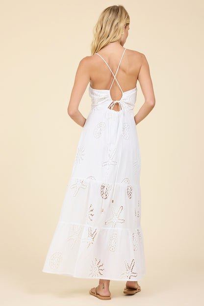 Woman wearing a white dress with floral eyelet embroidery on a beige background