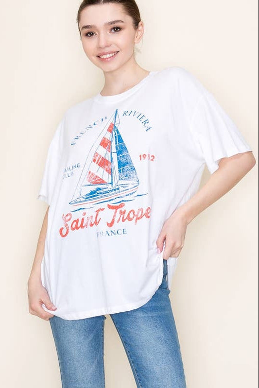 Person wearing a white t-shirt with a sailboat graphic and 'Saint Tropez' text on a plain background