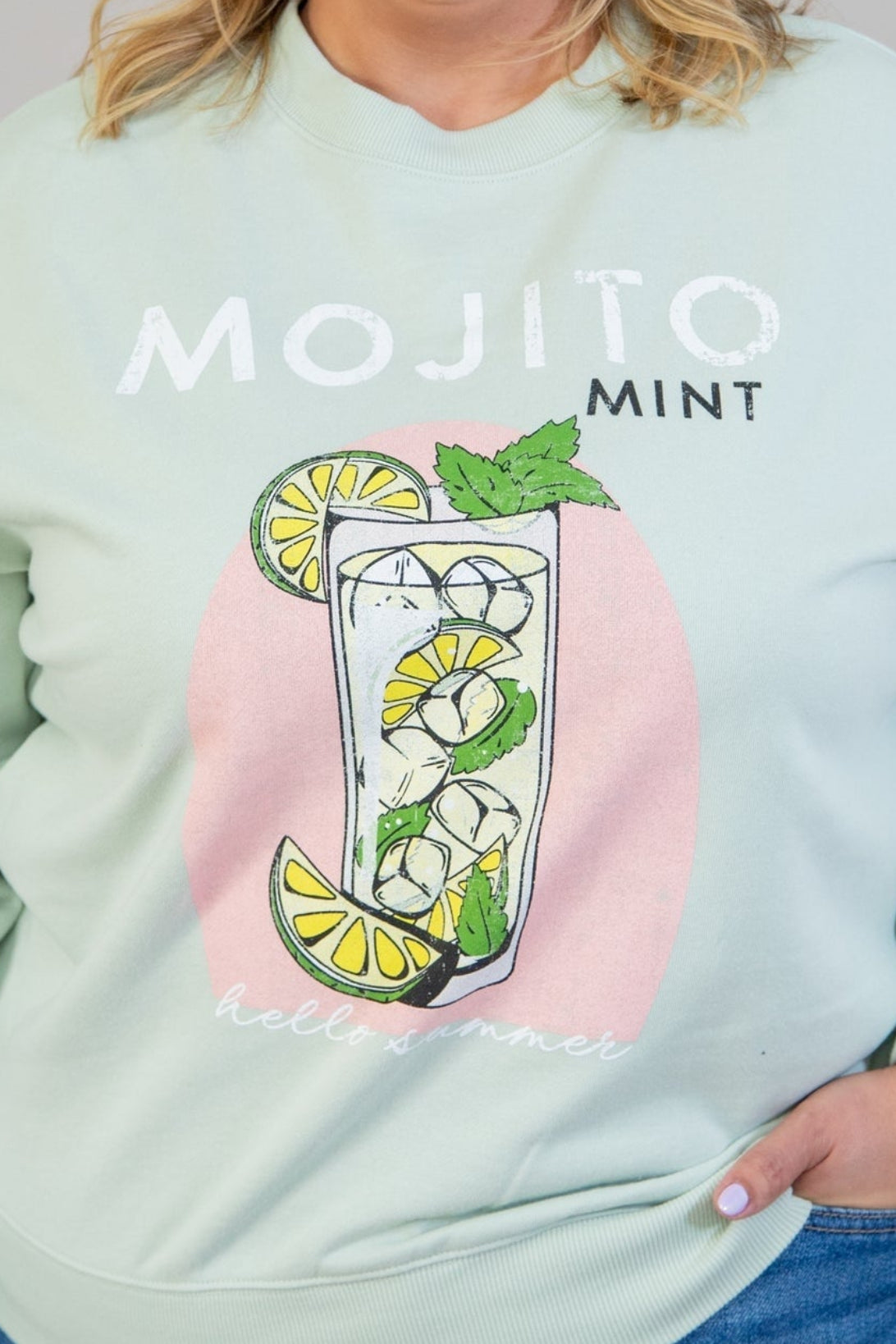 Person wearing a light green sweatshirt with 'Mojito Mint' design on a plain background