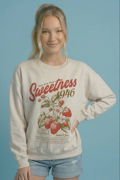 Ivory crewneck sweatshirt with 'Sweetness 1946' strawberry print, hand on hip
