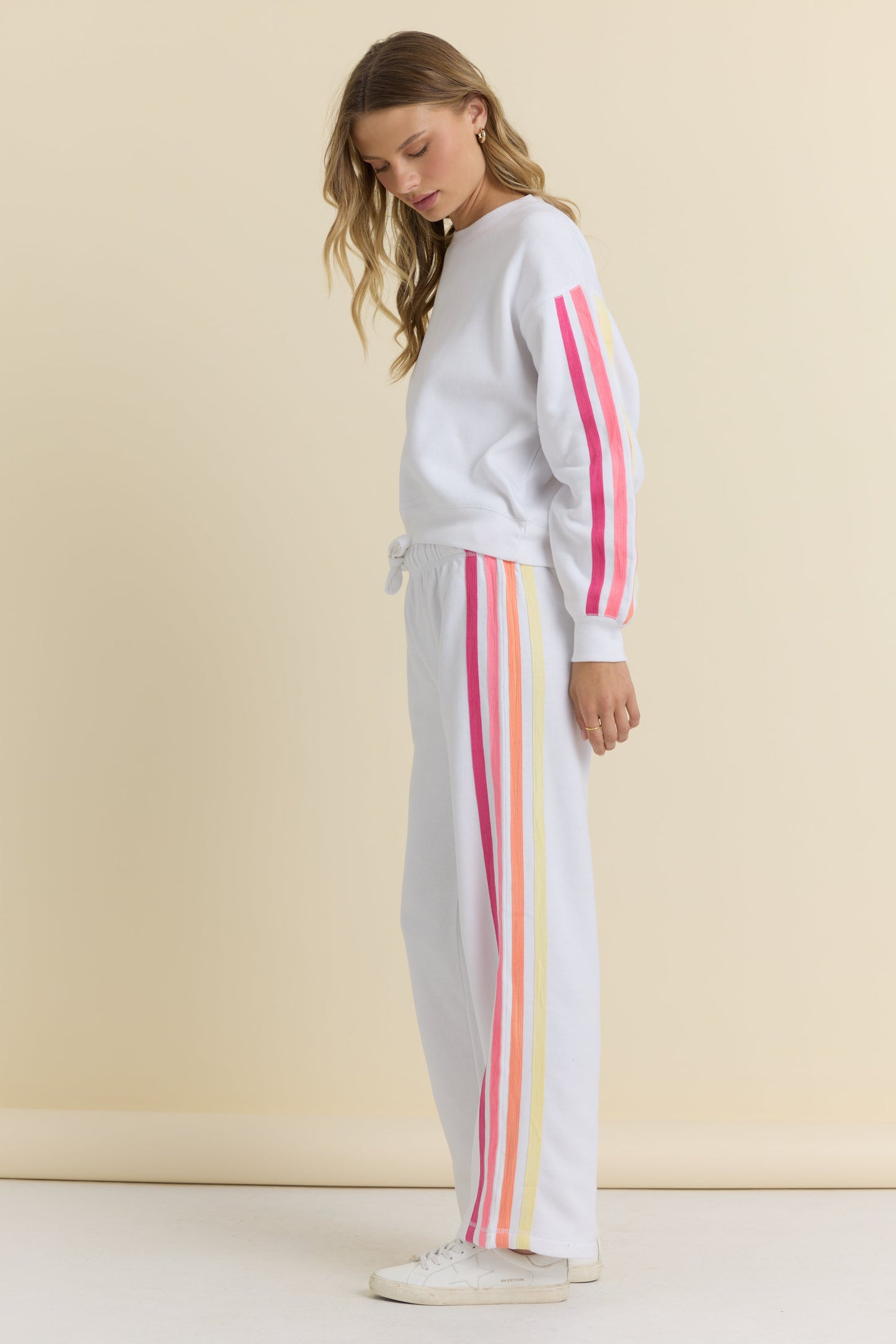 Woman wearing a white sweater and white pants with colorful stripes on a beige background