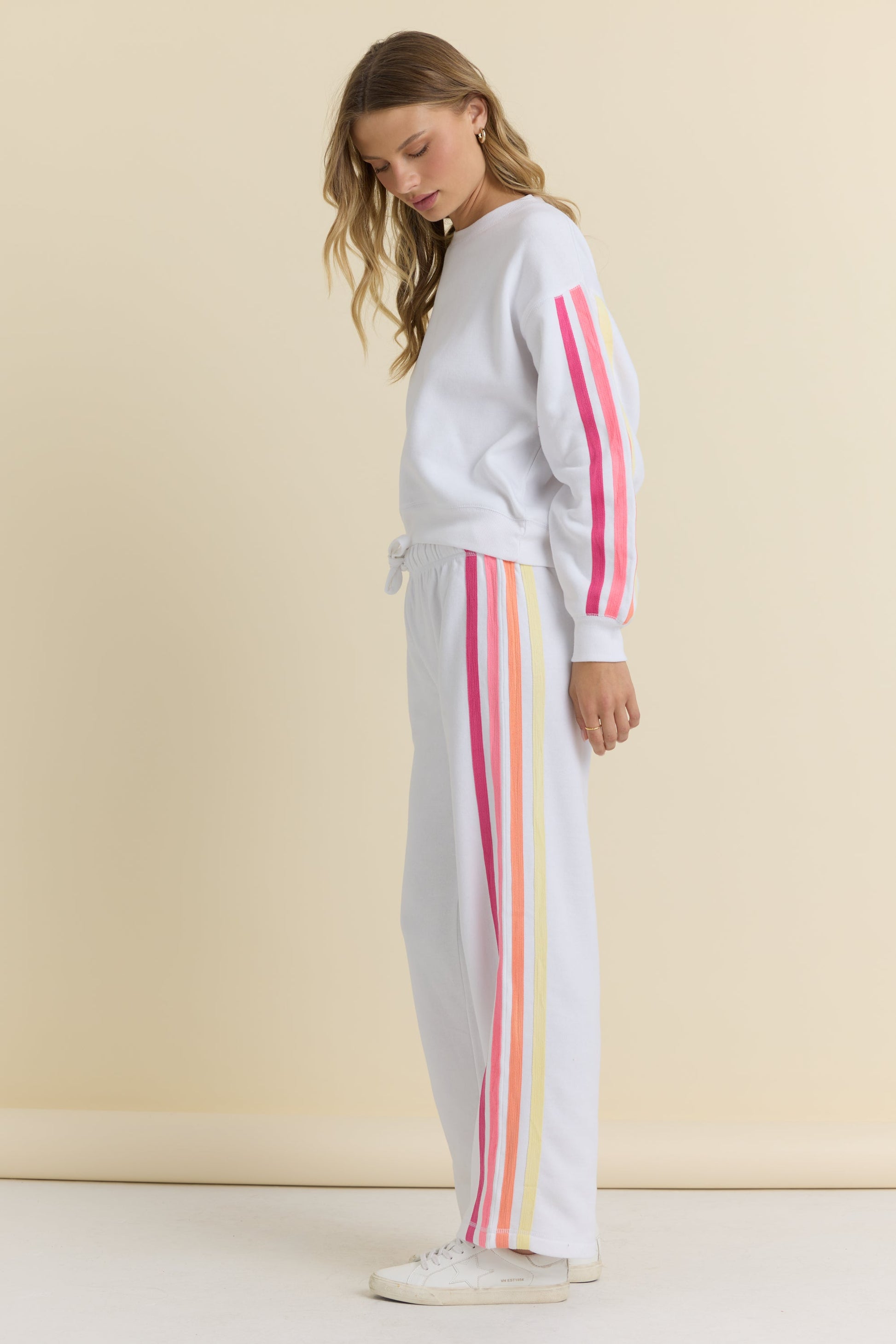 Woman wearing a white sweater and white pants with colorful stripes on a beige background