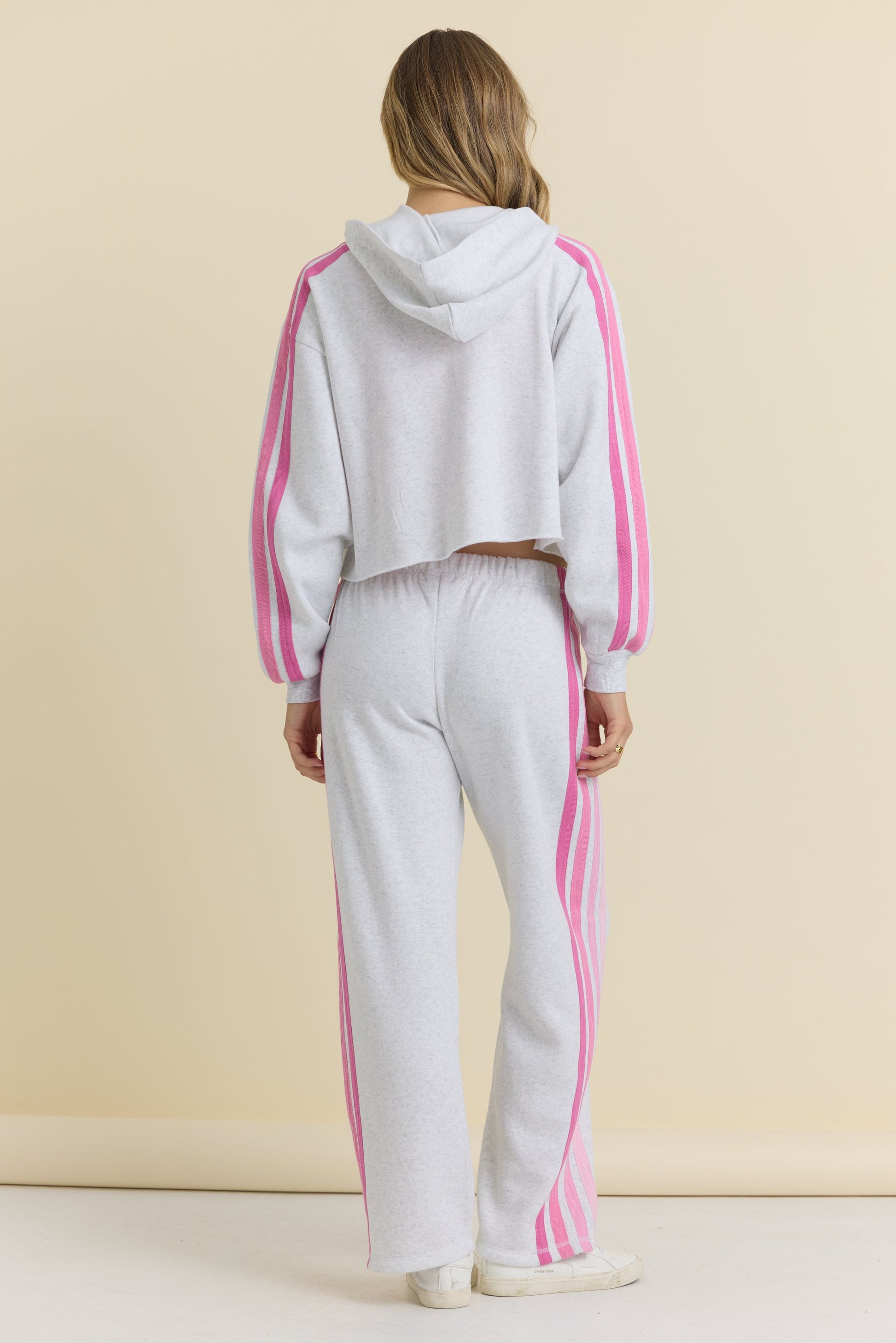 Person wearing a white tracksuit with pink stripes on a beige background