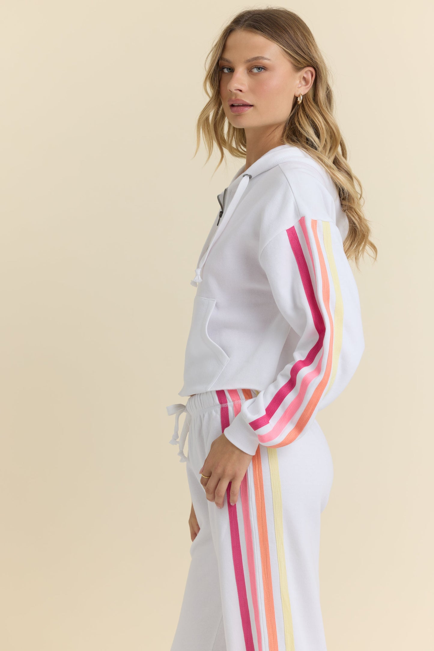 Woman wearing a white hoodie with colorful stripes on a beige background