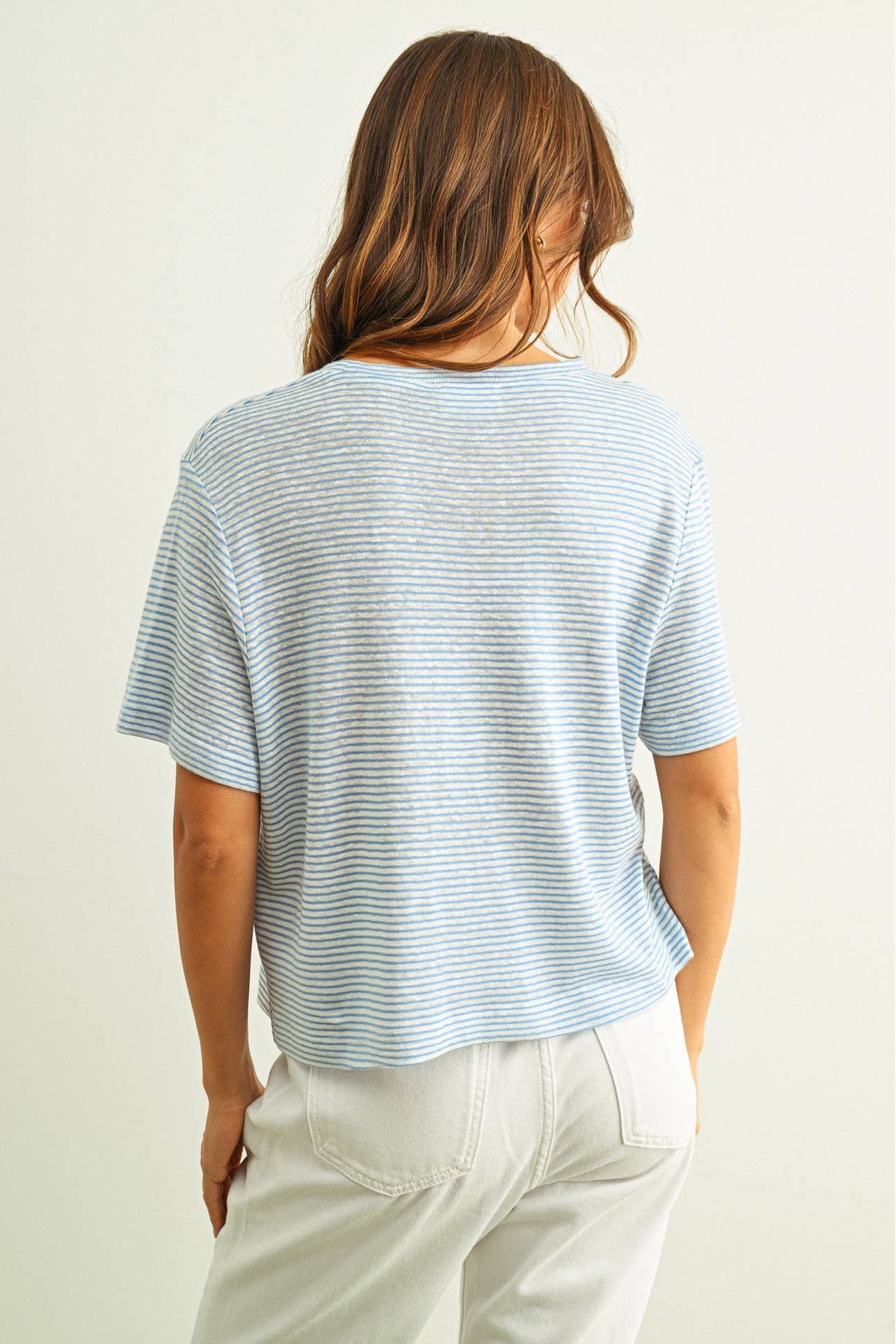 Person wearing a light blue striped slub tshirt and white pants against a plain background