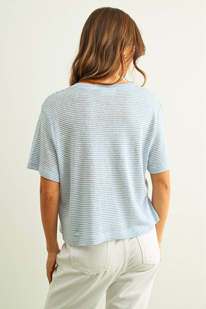 Person wearing a light blue striped slub tshirt and white pants against a plain background