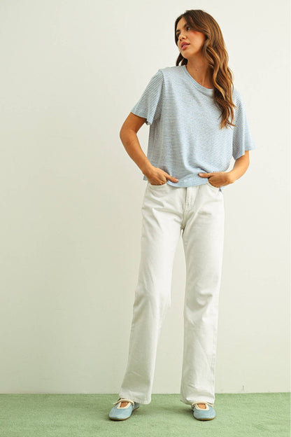 Woman wearing a light blue striped slub shirt and white pants against a plain background