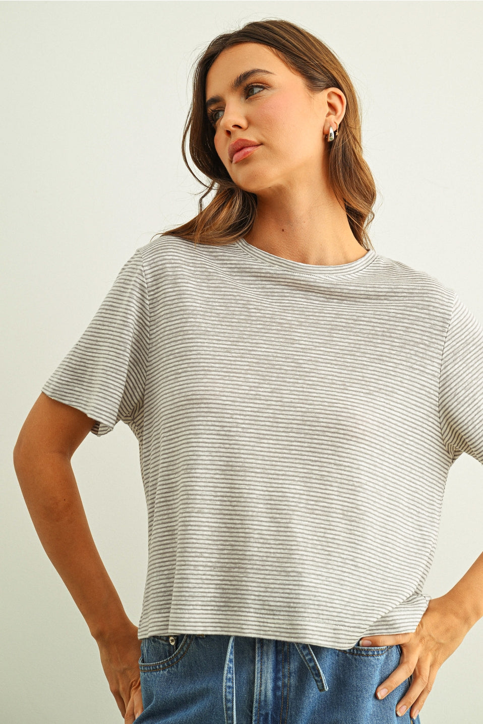 Woman wearing a grey & white striped t-shirt and jeans against a plain background