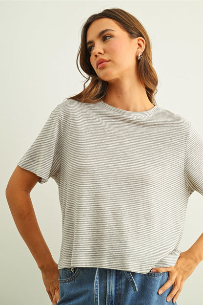 Woman wearing a grey & white striped t-shirt and jeans against a plain background