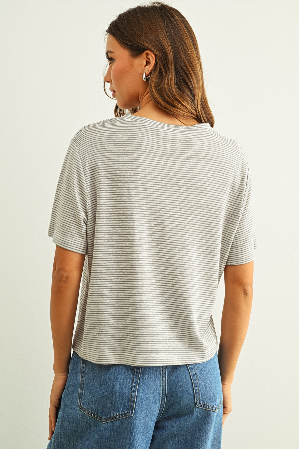 Back view of woman wearing a grey & white striped shirt and blue jeans on a plain background