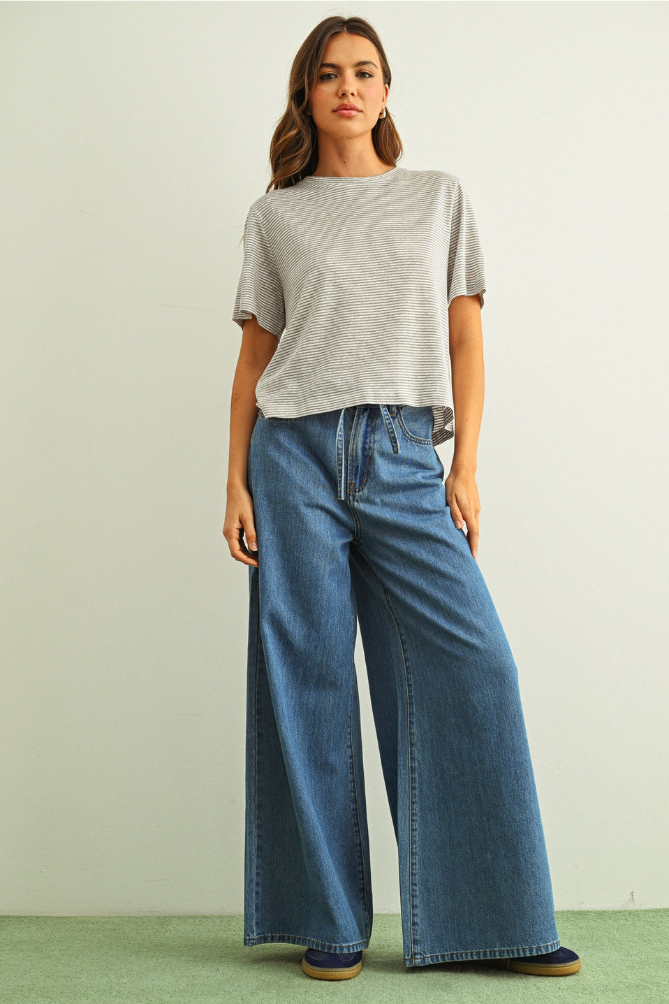 Woman wearing a gray striped slub t-shirt and blue jeans against a plain background